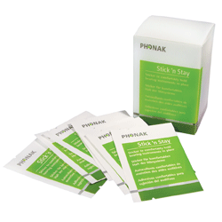 A box labeled Phonak Stick'n Stay stands behind several green and white packets spread out in front; the packaging is for Phonak Stick'n Stay hearing aid accessories.