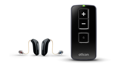 Two small behind-the-ear hearing aids with thin wires are next to an Oticon Remote Control 3.0, a rectangular black device with plus, minus, and central buttons.