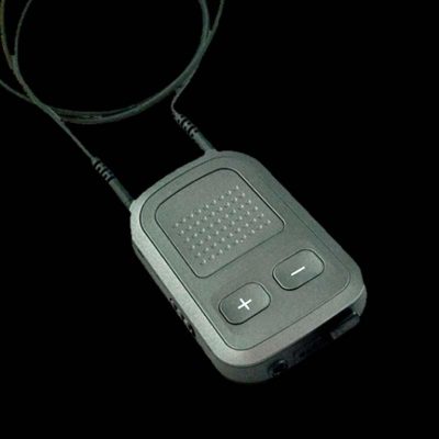 The Unitron uDirect 2 is a compact rectangular electronic device with a textured surface, two prominent plus and minus buttons, and attached wired earphones, all set against a black background.